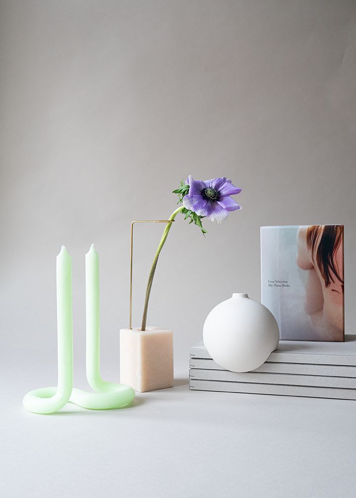 Design objects: green candles, white spherical vase and pink cube-shaped vase with a purple flower